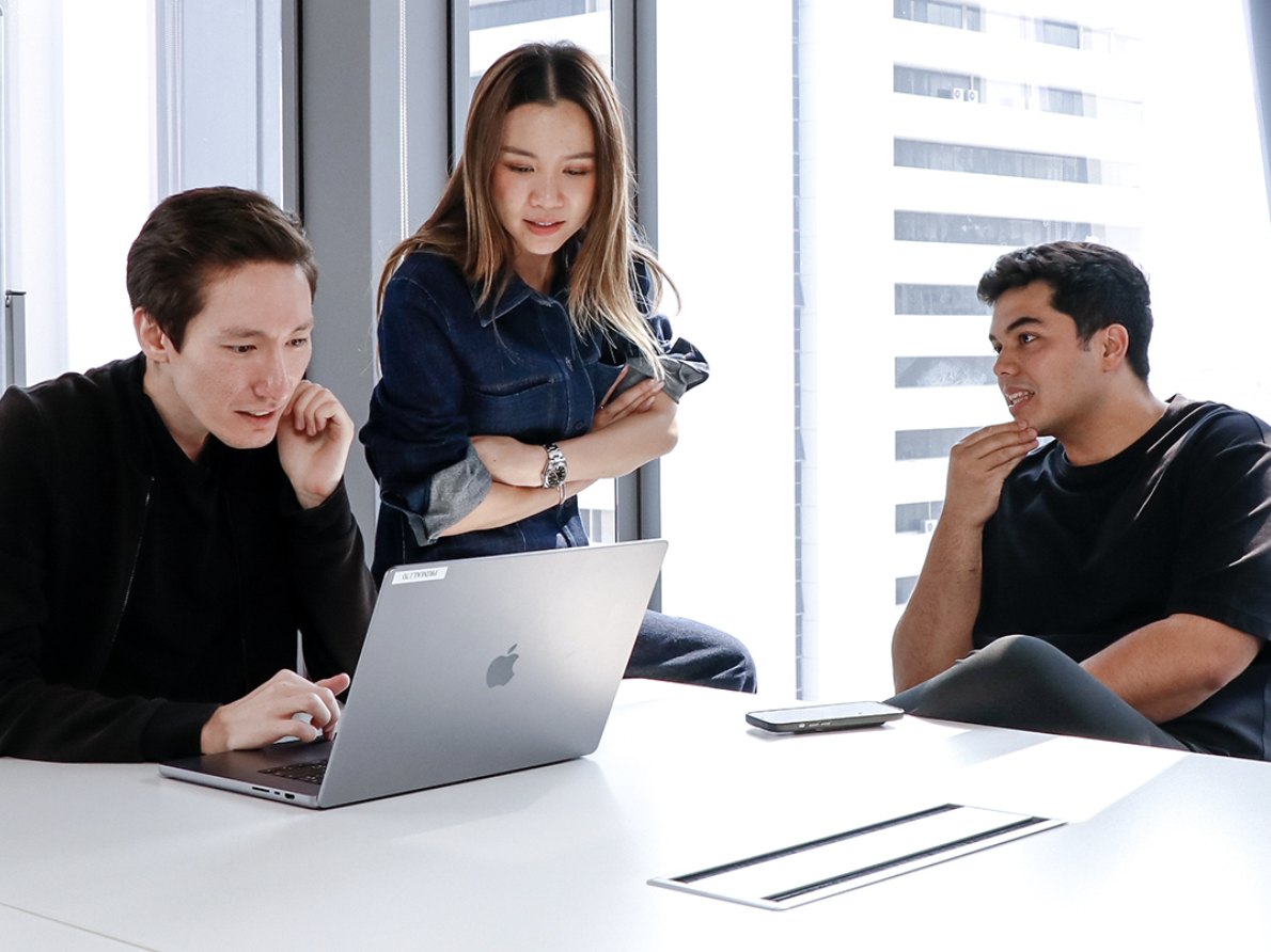 Three Primal colleagues looking at a laptop together at a white meeting table