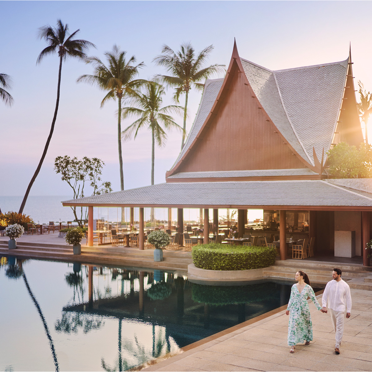 A Thai-style pavilion reflected in still water among palm trees