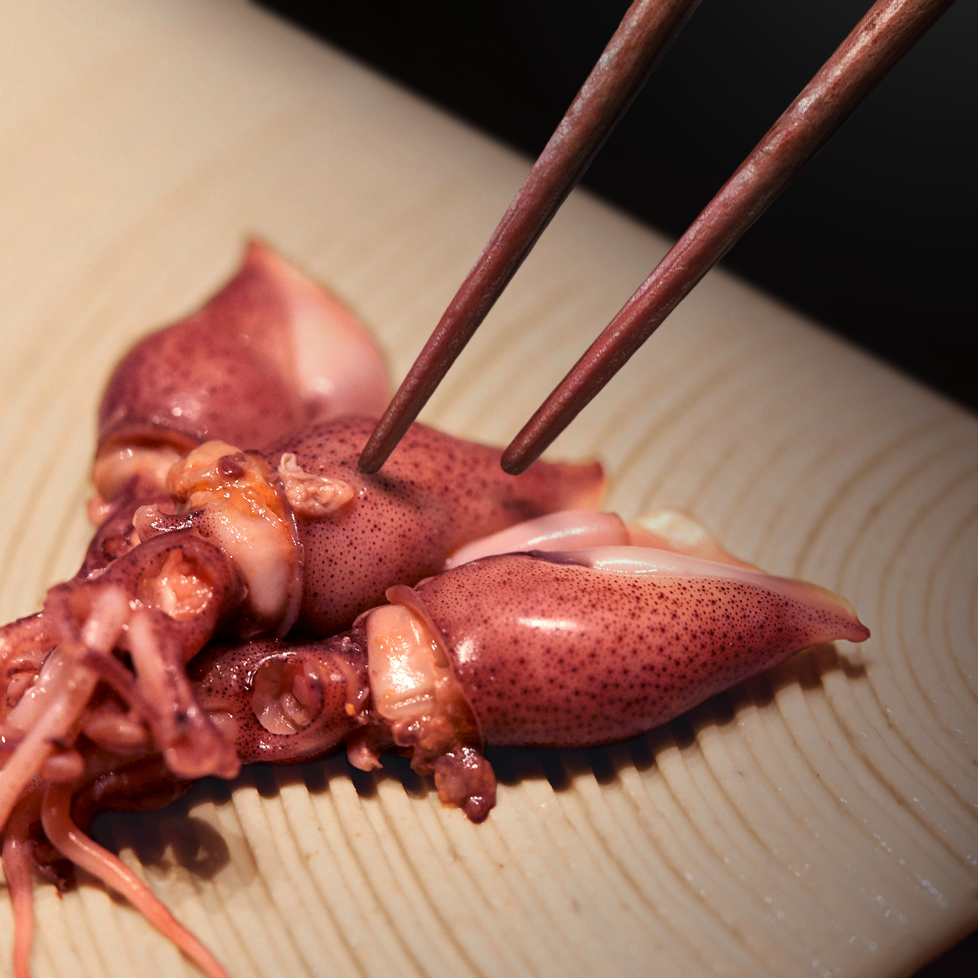 Chopsticks lifting a piece of grilled squid on a wooden board